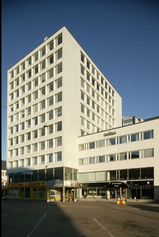 Valkoinen monikerroksinen rakennus, jonka katutasossa on liiketiloja.