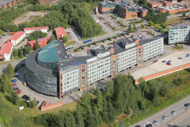 Ilmakuva suuresta modernista toimistorakennuksesta ja sen lähiympäristöstä.