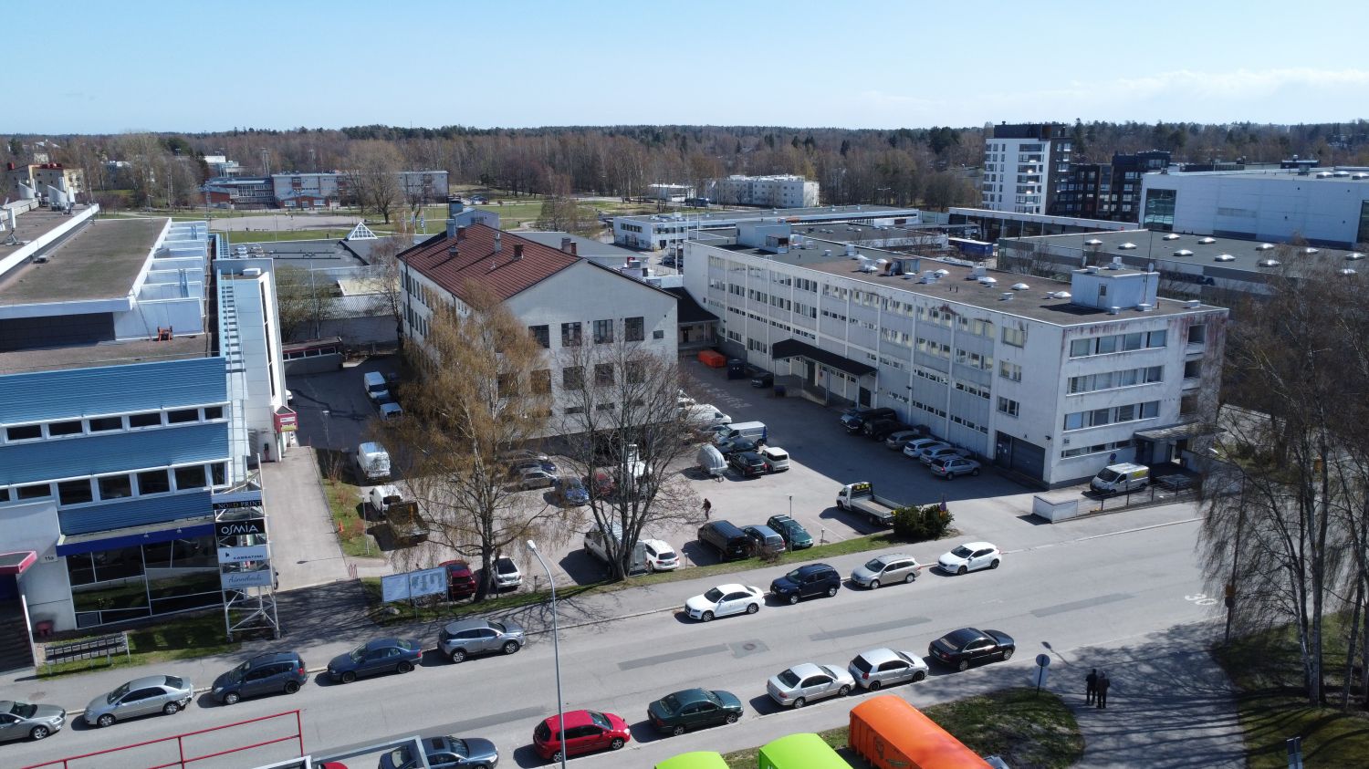 Ilmakuva teollisuus- ja liikealueesta, jossa on useita rakennuksia ja pysäköityjä autoja.