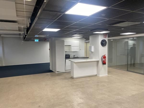 Avoin toimistotila, jossa on pieni keittiönurkkaus, saareke ja lasiseinäinen huone.