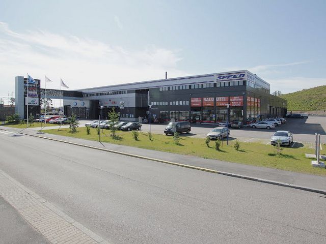 Suuri liikerakennus ja sen edessä oleva pysäköintialue autoineen aurinkoisena päivänä.
