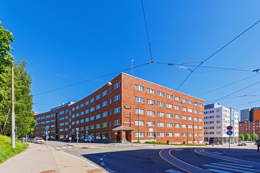 Punatiilinen rakennus ja raitiovaunukiskoja aurinkoisessa kaupunkimaisemassa.