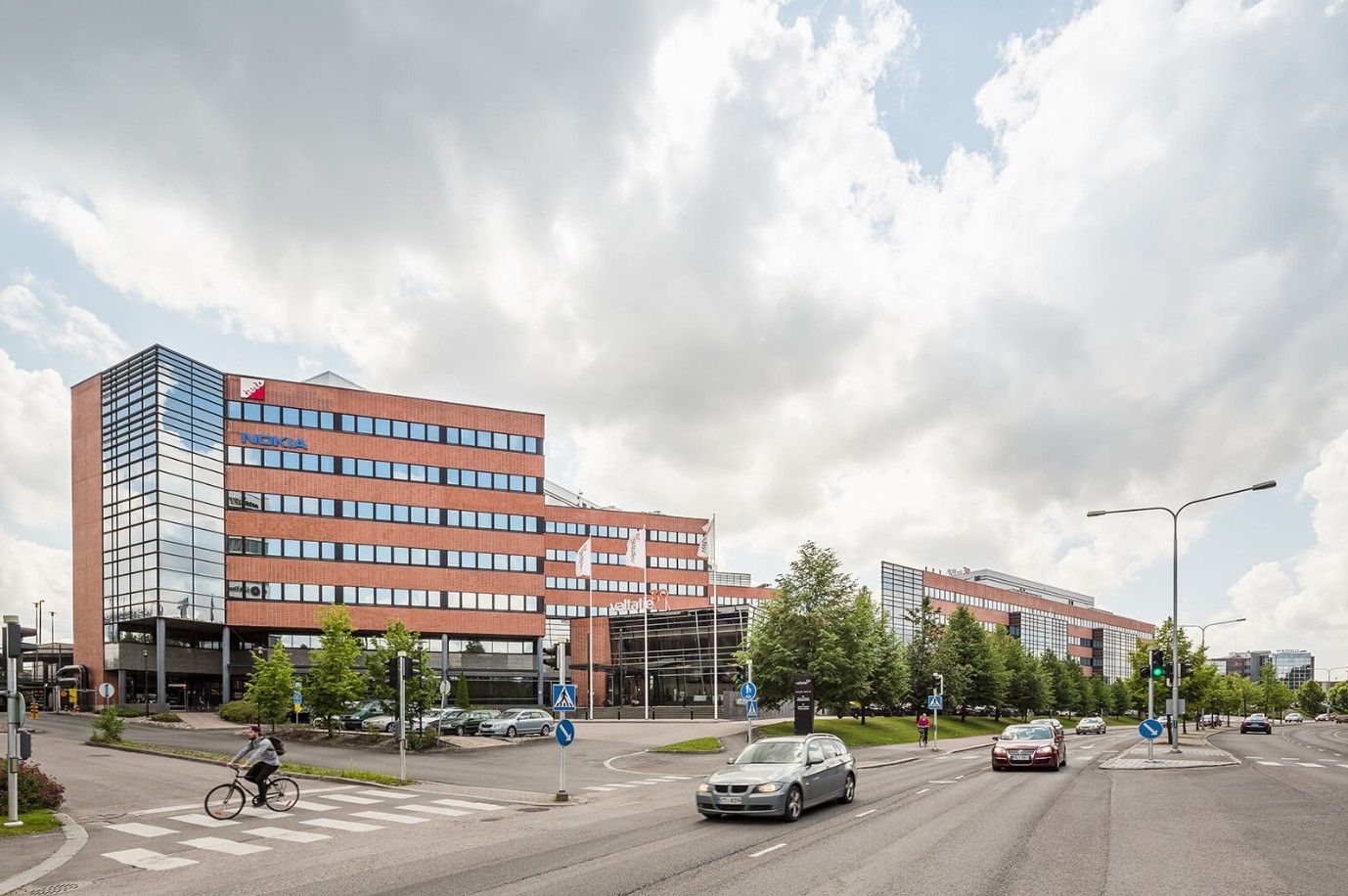 Moderni toimistorakennus ja katunäkymä, jossa on autoja ja pyöräilijä.