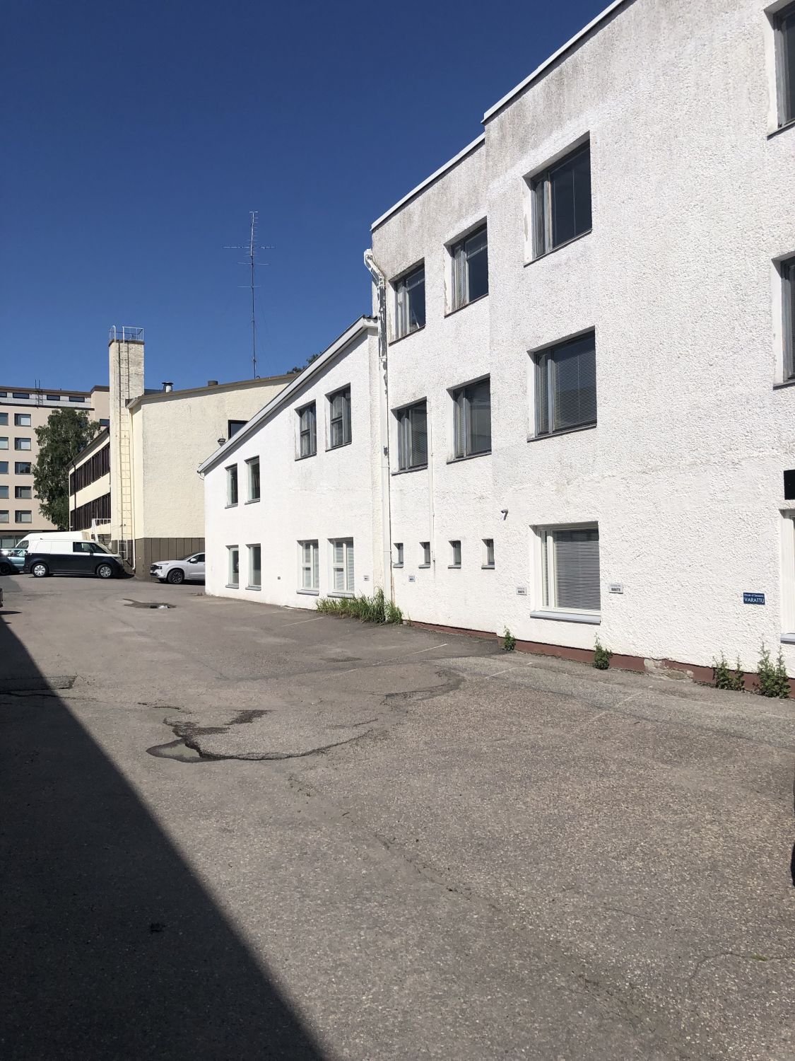 Valkoinen rakennus ja asfaltoitu piha-alue aurinkoisena päivänä.