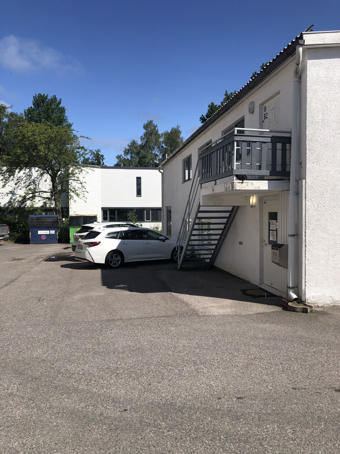 Valkoinen auto pysäköitynä valkoisen rakennuksen eteen, jossa on metalliset ulkoportaat.