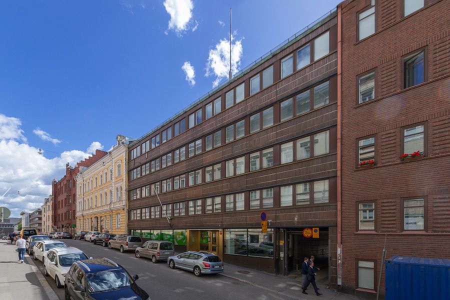 Kaupunkinäkymä kadulta, jonka varrella on rakennuksia ja pysäköityjä autoja.