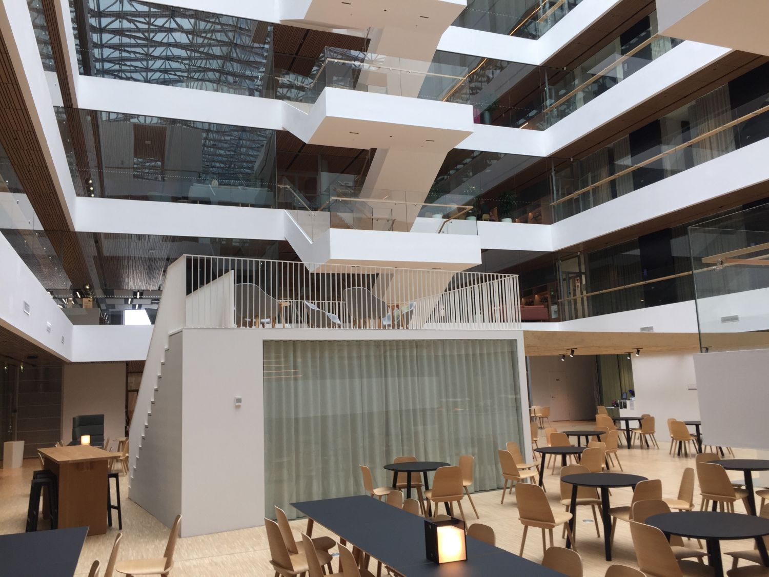 Modernin rakennuksen avara atrium-tila, jossa on monitasoisia portaikkoja ja istumaryhmiä.