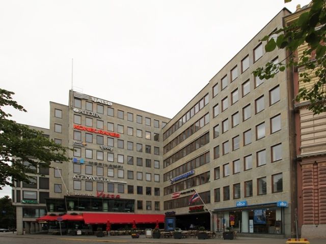 Monikerroksinen toimistorakennus, jonka julkisivussa on useita yritysten logoja ja katutasossa ra...