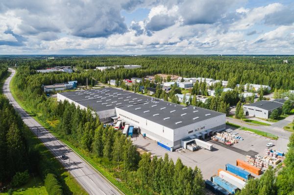 Ilmakuva suuresta teollisuusrakennuksesta metsän ympäröimänä.