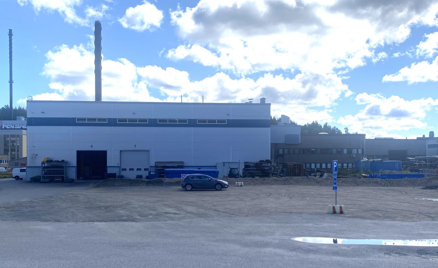 Teollisuusrakennus ja sen pihalla pysäköity auto aurinkoisena päivänä.