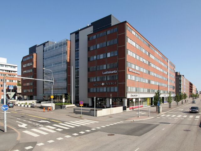 Monikerroksinen toimistorakennus kaupungin kadun kulmassa aurinkoisena päivänä.