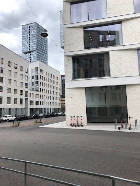 Moderni kaupunkinäkymä, jossa on vaaleita rakennuksia, sähköpotkulautoja ja korkea tornitalo taus...