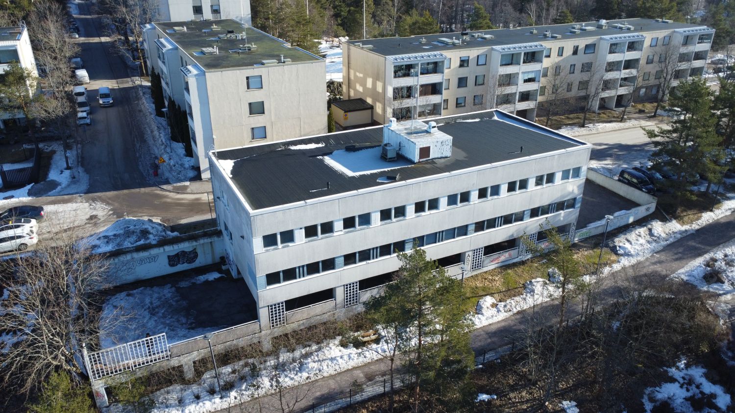 Ilmakuva asuinalueen rakennuksista ja sulavasta lumesta aurinkoisena päivänä.