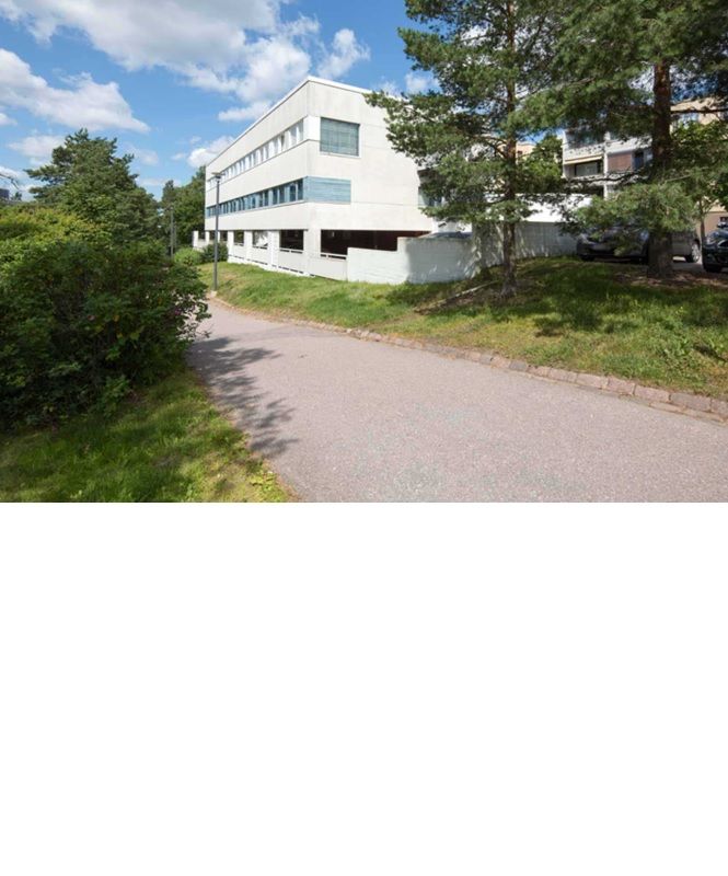Valkoinen rakennus asfaltoidun tien varrella puiden ympäröimänä.