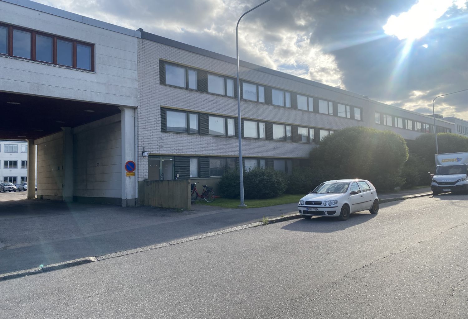 Valkoinen liikerakennus kadun varrella ja sen edessä pysäköity valkoinen henkilöauto.