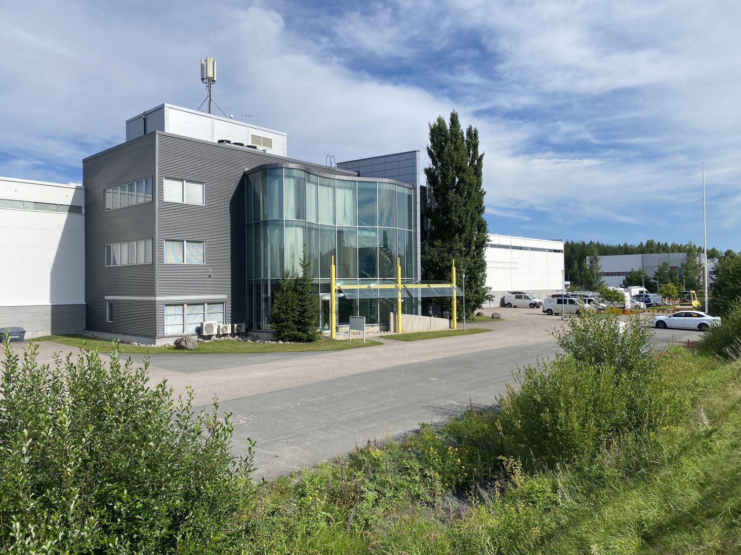 Moderni toimisto- tai teollisuusrakennus, jossa on kaareva lasijulkisivu ja harmaa ulkoverhoilu.