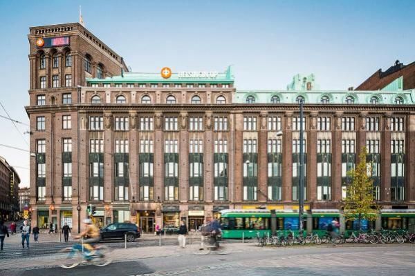 Kaupunkinäkymä Helsingistä, jossa on historiallinen rakennus ja vihreä raitiovaunu.